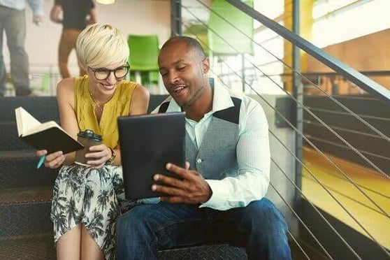 Two people sitting at the stairs, looking at a tablet.